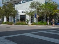 a man crossing the street with his skateboard, in front of the dojo building