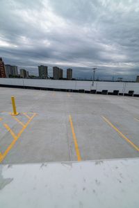 a parking lot with two yellow lines painted on the concrete area with tall buildings in the distance