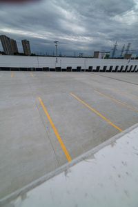 a parking lot with two yellow lines painted on the concrete area with tall buildings in the distance