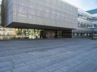 a very large building that is on a road side walk area with glass windows and concrete steps