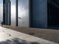 a man stands outside in the shadows with his skateboard on the sidewalk outside of a large building