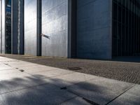 a man stands outside in the shadows with his skateboard on the sidewalk outside of a large building