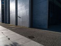 a man stands outside in the shadows with his skateboard on the sidewalk outside of a large building