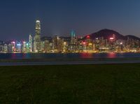 a city skyline is illuminated in the evening time light as well as grass, by the sea and hill