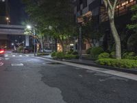 the road to an apartment is empty at night with bright lighting on it and several trees surrounding