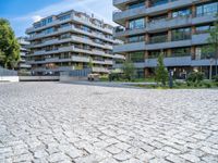 the modern apartment block is next to an empty sidewalk and sidewalk with a stone bench near by it