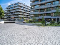 the modern apartment block is next to an empty sidewalk and sidewalk with a stone bench near by it