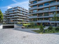 the modern apartment block is next to an empty sidewalk and sidewalk with a stone bench near by it