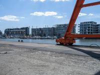 a crane moving in to shore of a marina next to a body of water with buildings