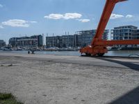 a crane moving in to shore of a marina next to a body of water with buildings