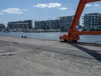 a crane moving in to shore of a marina next to a body of water with buildings