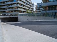 a street with an empty parking area between tall buildings and trees on the opposite side