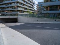 a street with an empty parking area between tall buildings and trees on the opposite side