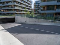 a street with an empty parking area between tall buildings and trees on the opposite side