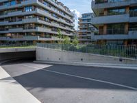 a street with an empty parking area between tall buildings and trees on the opposite side