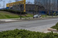 street view of a city and business complex on the corner of a hill with bushes in front