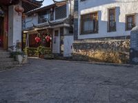 a small oriental courtyard with lanterns and building fronts in the background and the sun shining on the top of the roof