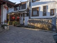 a small oriental courtyard with lanterns and building fronts in the background and the sun shining on the top of the roof