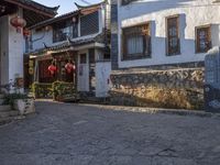 a small oriental courtyard with lanterns and building fronts in the background and the sun shining on the top of the roof