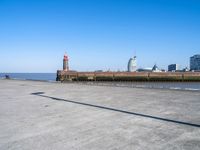 a woman walking down the sidewalk to a lighthouse and clock tower in an empty lot