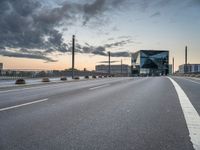 empty road with tall poles and modern glass building in background under stormy sky at dusk