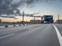 empty road with tall poles and modern glass building in background under stormy sky at dusk