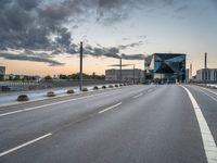 empty road with tall poles and modern glass building in background under stormy sky at dusk