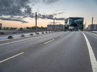 empty road with tall poles and modern glass building in background under stormy sky at dusk