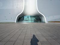 a white building with a glass window and tile in the courtyard with benches, pots, flower beds and other outdoor seating