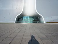 a white building with a glass window and tile in the courtyard with benches, pots, flower beds and other outdoor seating