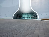 a white building with a glass window and tile in the courtyard with benches, pots, flower beds and other outdoor seating