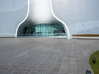 a white building with a glass window and tile in the courtyard with benches, pots, flower beds and other outdoor seating