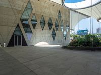 a concrete wall with geometric shaped windows and an open air parking area in front of it