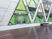 a green building with a bench in front of it on wooden floors and concrete, under glass windows