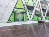 a green building with a bench in front of it on wooden floors and concrete, under glass windows