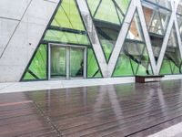 a green building with a bench in front of it on wooden floors and concrete, under glass windows