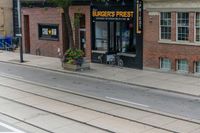 a man on a bike passes a burgers frisbee shop on a city street