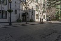 three people walking down the sidewalk on either side of a white building, some black trees and many tall buildings