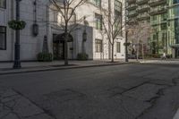 three people walking down the sidewalk on either side of a white building, some black trees and many tall buildings