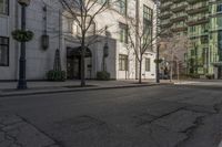 three people walking down the sidewalk on either side of a white building, some black trees and many tall buildings