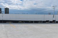 a car park with a white building in the background and cars parked below it and overhead sky with clouds