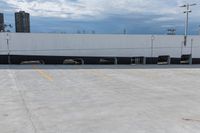 a car park with a white building in the background and cars parked below it and overhead sky with clouds