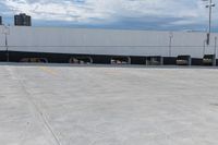 a car park with a white building in the background and cars parked below it and overhead sky with clouds