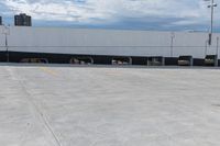 a car park with a white building in the background and cars parked below it and overhead sky with clouds