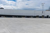 a car park with a white building in the background and cars parked below it and overhead sky with clouds