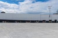 a car park with a white building in the background and cars parked below it and overhead sky with clouds