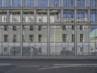 a large building is reflected in the side of the street that goes along this narrow road