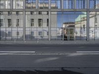 a large building is reflected in the side of the street that goes along this narrow road