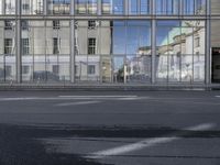 a large building is reflected in the side of the street that goes along this narrow road