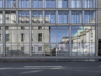 a large building is reflected in the side of the street that goes along this narrow road